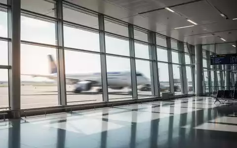 Ein modernes, helles Flughafenterminal mit großen Fenstern und einem unscharfen Flugzeug im Hintergrund. - Foto: über boerse-global.de