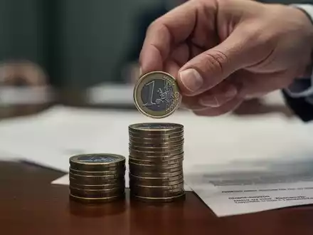 Eine Hand legt eine Euromünze auf einen Stapel, symbolisch für die Debatte um Bürgergeld und soziale Absicherung. - Foto: über boerse-global.de