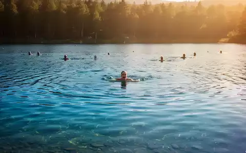Ein ruhiger, klarer See bei Sonnenuntergang mit badenden Menschen in der Ferne, der die Sommerhitze und die Gefahren beim Schwimmen symbolisiert. - Foto: über boerse-global.de