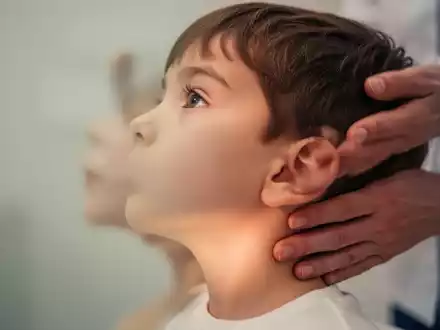 Ein Kind im Profil, dessen Kiefer- und Nackenbereich im Fokus liegt, mit einer unscharfen Hand eines Erwachsenen in der Nähe. - Foto: über boerse-global.de