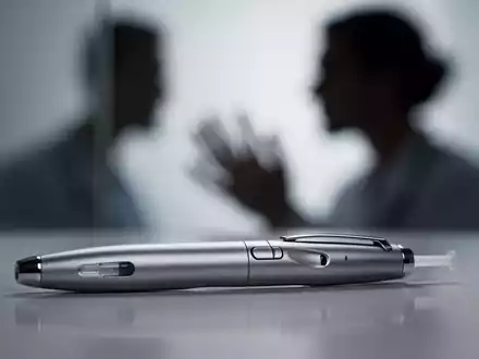 Eine Nahaufnahme eines modernen Injektionspens mit unscharfem Hintergrund, der eine Person andeutet, die den Stift betrachtet. - Foto: über boerse-global.de