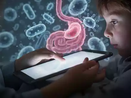 Nahaufnahme einer Kinderhand, die ein leuchtendes Tablet hält, mit unscharfen, abstrakten Bakterienformen im Hintergrund. - Foto: über boerse-global.de