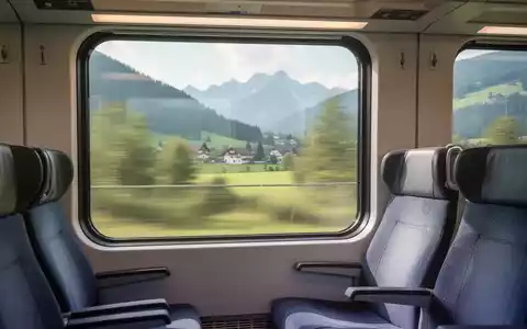 Innenansicht eines modernen Zuges mit Blick aus dem Fenster auf eine verschwommene bayerische Landschaft, leere Sitze im Vordergrund. - Foto: über boerse-global.de