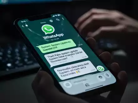 Nahaufnahme eines Smartphones mit einer betrügerischen WhatsApp-Nachricht und unscharfen Händen, die auf einer Tastatur tippen. - Foto: über boerse-global.de