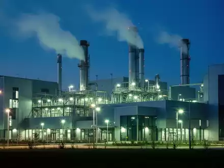 Eine moderne Industrieanlage mit leuchtenden, energieeffizienten Lichtern und subtilem Rauch aus Schornsteinen bei Dämmerung. - Foto: über boerse-global.de