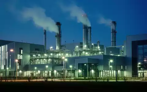 Eine moderne Industrieanlage mit leuchtenden, energieeffizienten Lichtern und subtilem Rauch aus Schornsteinen bei Dämmerung. - Foto: über boerse-global.de