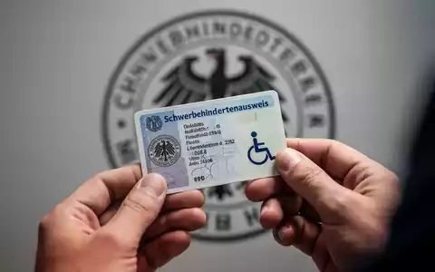Hände halten einen deutschen Schwerbehindertenausweis, im Hintergrund verschwommenes Behördensiegel, das Verwaltungsprozesse andeutet. - Foto: über boerse-global.de
