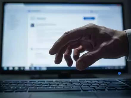 Hand hovering over a computer keyboard, with a blurred screen displaying an email interface in the background. - Foto: über boerse-global.de