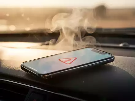 Ein Smartphone liegt auf einem Armaturenbrett eines Autos, umgeben von Hitzeflimmern, unter direkter Sonneneinstrahlung. - Foto: über boerse-global.de