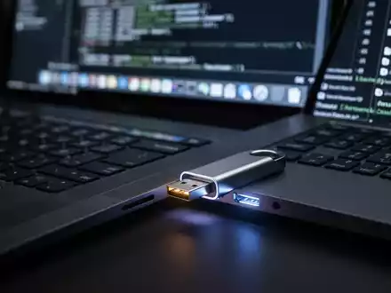 A close-up of a USB drive plugged into a laptop keyboard, with a blurred screen in the background showing technical code. - Foto: über boerse-global.de
