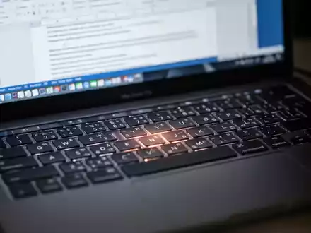 Close-up of a MacBook Pro keyboard with a blurred Microsoft Word document open on the screen in the background. - Foto: über boerse-global.de
