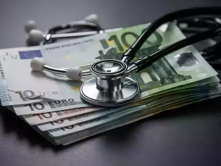 Ein Stapel Euro-Banknoten, teilweise verdeckt von einem Stethoskop, symbolisiert die steigenden Gesundheitsausgaben und die GKV-Reform. - Foto: über boerse-global.de