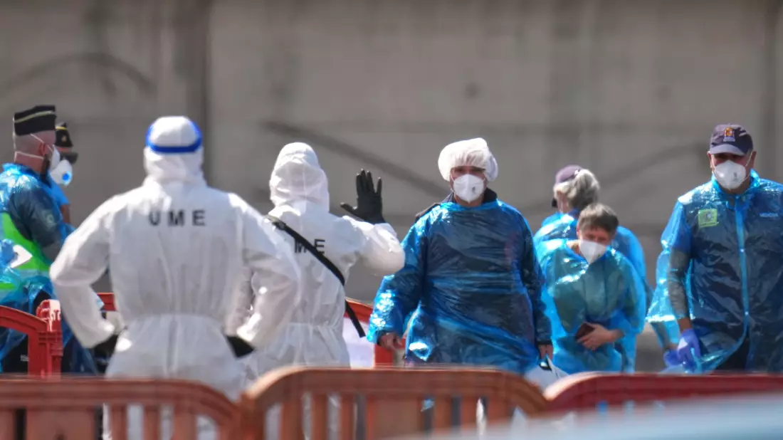 Personen in Schutzbekleidung und mit Masken (r) gehen im Hafen von Granadilla auf Teneriffa an Land, nachdem sie mit einem Boot von dem vom Hantavirus betroffenen Kreuzfahrtschiff MV Hondius gebracht wurden - Bild: Manu Fernandez/AP/dpa