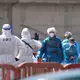 Personen in Schutzbekleidung und mit Masken (r) gehen im Hafen von Granadilla auf Teneriffa an Land, nachdem sie mit einem Boot von dem vom Hantavirus betroffenen Kreuzfahrtschiff MV Hondius gebracht wurden - Bild: Manu Fernandez/AP/dpa