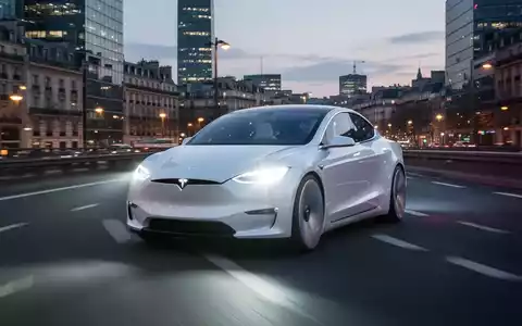 A sleek white autonomous electric car, resembling a Tesla, drives on a highway through a modern European city at dusk. - Foto: über boerse-global.de