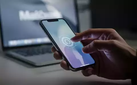 A hand tapping an iPhone screen, with a MacBook in the blurred background, illustrating wireless unlocking technology. - Foto: über boerse-global.de