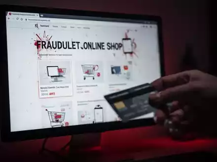 Ein unscharfer Computerbildschirm zeigt einen betrügerischen Online-Shop, eine Hand greift nach einer Kreditkarte. Symbolisiert Online-Betrug. - Foto: über boerse-global.de