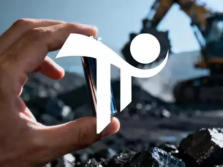 Eine Hand hält eine Lithium-Ionen-Batteriezelle vor einem unscharfen Hintergrund mit Bergbauausrüstung. - Foto: über boerse-global.de