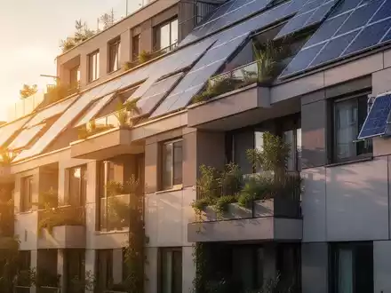 Eine moderne, energieeffiziente Wohnhausfassade mit Solarpanelen und grünen Elementen, beleuchtet von warmer Sonne. - Foto: über boerse-global.de