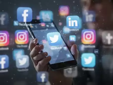 Eine junge Person hält ein Smartphone; im unscharfen Hintergrund sind mehrere Social-Media-App-Symbole zu sehen. - Foto: über boerse-global.de