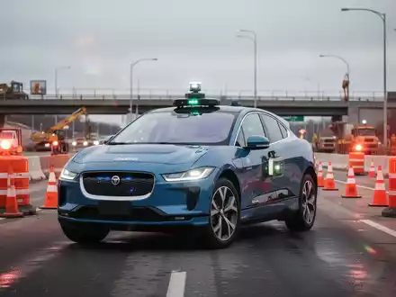 A Waymo robotaxi (Jaguar I-Pace) stopped at the entrance of a highway construction zone with cones and flashing lights. - Foto: über boerse-global.de