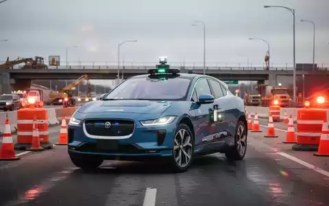A Waymo robotaxi (Jaguar I-Pace) stopped at the entrance of a highway construction zone with cones and flashing lights. - Foto: über boerse-global.de