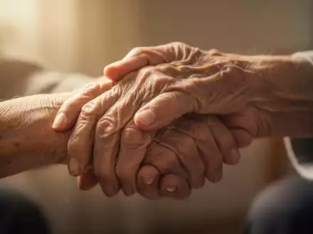 Eine pflegende Hand hält sanft die Hand eines älteren Menschen, was häusliche Demenzpflege und ihre Herausforderungen symbolisiert. - Foto: über boerse-global.de