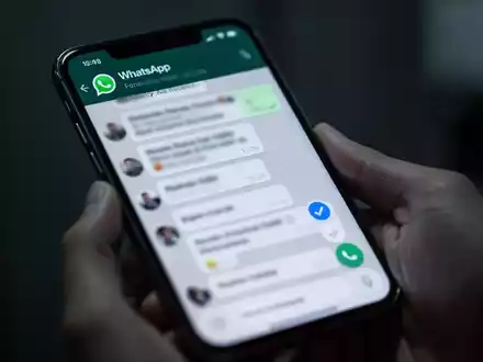 Close-up of a hand holding a smartphone displaying a WhatsApp chat, with a blue checkmark visible on the screen. - Foto: über boerse-global.de