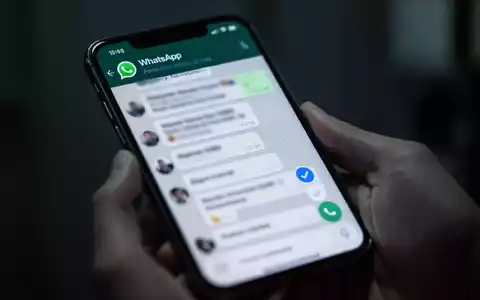 Close-up of a hand holding a smartphone displaying a WhatsApp chat, with a blue checkmark visible on the screen. - Foto: über boerse-global.de