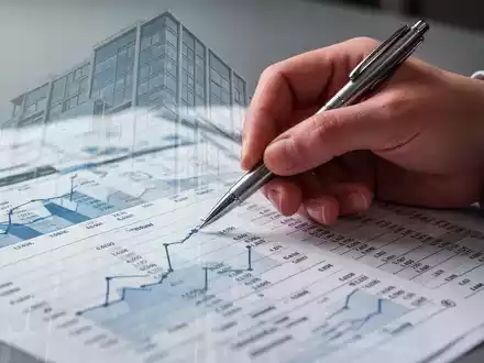 Nahaufnahme einer Hand, die mit einem Stift auf ein Finanzdokument zeigt, mit einer subtilen Überlagerung eines modernen Gebäudes. - Foto: über boerse-global.de