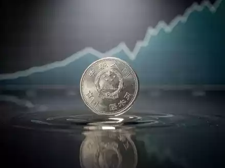 Eine einzelne chinesische Yuan-Münze fällt auf eine dunkle, spiegelnde Oberfläche, mit einem unscharfen Diagramm im Hintergrund. - Foto: über boerse-global.de
