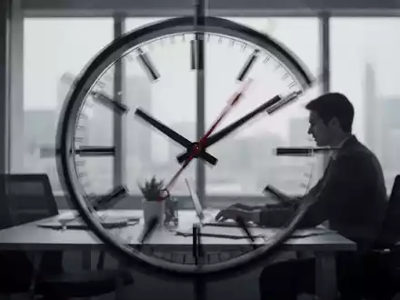 Eine stilisierte Uhr mit unscharfen Zeigern, die schnell vergehende Zeit andeutet. Im Hintergrund arbeitet eine Person. - Foto: über boerse-global.de