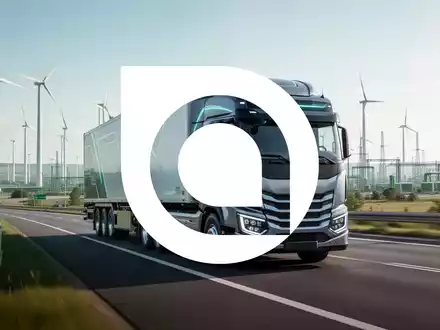 Ein emissionsfreier Wasserstoff-Lkw fährt auf einer Autobahn in einer modernen Industrielandschaft mit Windturbinen im Hintergrund. - Foto: über boerse-global.de