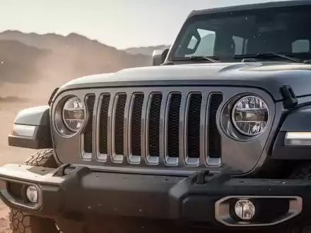 Nahaufnahme des Kühlergrills eines modernen Jeep Wrangler in einer sonnigen Wüstenlandschaft, Scheinwerfer an. - Foto: über boerse-global.de