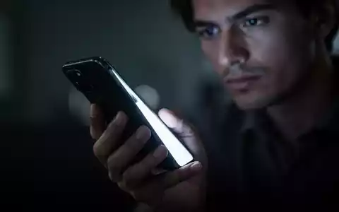Eine Hand hält ein leuchtendes Smartphone in einer verschwommenen, dunklen Umgebung, die digitale Ablenkung symbolisiert. - Foto: über boerse-global.de