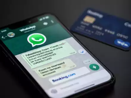 Nahaufnahme eines Smartphones mit einer WhatsApp-Nachricht, die eine gefälschte Booking.com-Oberfläche zeigt, im Hintergrund eine unscharfe Kreditkarte. - Foto: über boerse-global.de