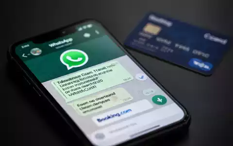 Nahaufnahme eines Smartphones mit einer WhatsApp-Nachricht, die eine gefälschte Booking.com-Oberfläche zeigt, im Hintergrund eine unscharfe Kreditkarte. - Foto: über boerse-global.de