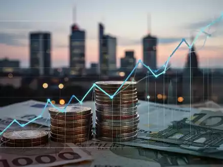 Nahaufnahme von Euro-Münzen und -Banknoten, teilweise verdeckt von einem aufsteigenden Liniendiagramm, vor einer verschwommenen deutschen Stadtkulisse. - Foto: über boerse-global.de