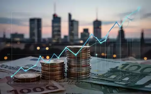 Nahaufnahme von Euro-Münzen und -Banknoten, teilweise verdeckt von einem aufsteigenden Liniendiagramm, vor einer verschwommenen deutschen Stadtkulisse. - Foto: über boerse-global.de