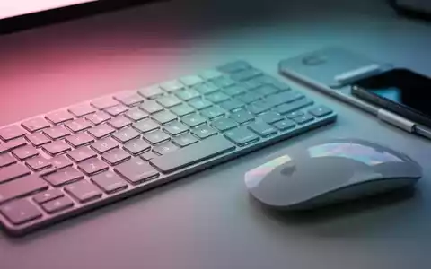 Apple Magic Keyboard and Mouse with a thin MagSafe grip, bathed in soft pink, teal, and blue light. - Foto: über boerse-global.de