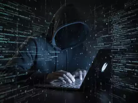A person in a hoodie typing on a laptop with digital code and data streams, symbolizing a cyber threat and data theft. - Foto: über boerse-global.de
