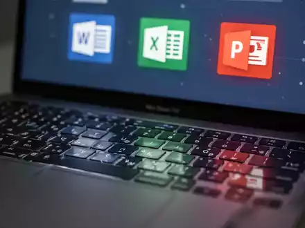 Close-up of a MacBook keyboard with a blurred screen displaying Microsoft Office application icons like Word, Excel, and PowerPoint. - Foto: über boerse-global.de