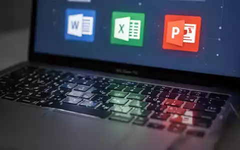 Close-up of a MacBook keyboard with a blurred screen displaying Microsoft Office application icons like Word, Excel, and PowerPoint. - Foto: über boerse-global.de