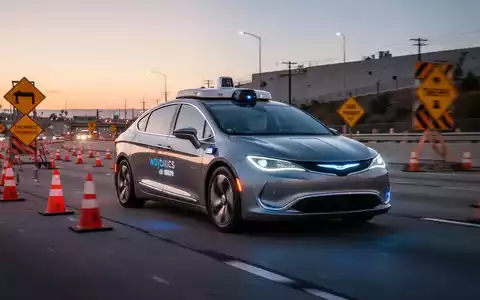 A Waymo self-driving car navigating through a freeway construction zone with orange cones and signs at dusk. - Foto: über boerse-global.de