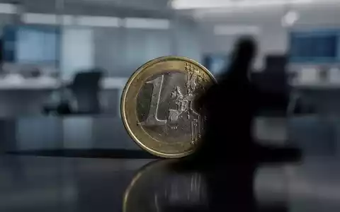 Eine einzelne stilisierte Euromünze, teilweise von einem Schatten verdeckt, auf einer reflektierenden Oberfläche in einem Finanzbüro. - Foto: über boerse-global.de