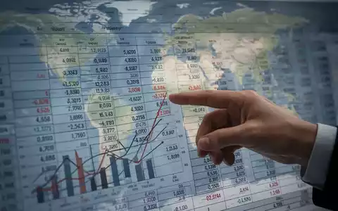 Eine Hand zeigt auf einen Finanzbericht mit Zahlen und Diagrammen, im Hintergrund eine angedeutete Weltkarte. - Foto: über boerse-global.de