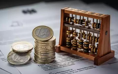 Ein Stapel deutscher Euro-Münzen neben einem Abakus, mit verschwommenen Dokumenten im Hintergrund, symbolisiert finanzielle Berechnungen und Beiträge. - Foto: über boerse-global.de