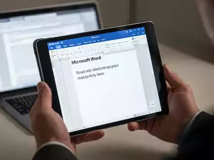 A person's hands holding an iPad displaying a Microsoft Word document in a read-only mode, with a blurred MacBook in the background. - Foto: über boerse-global.de