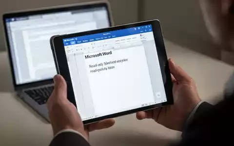 A person's hands holding an iPad displaying a Microsoft Word document in a read-only mode, with a blurred MacBook in the background. - Foto: über boerse-global.de