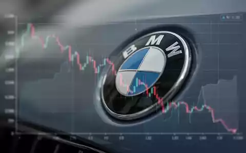 Nahaufnahme eines BMW-Logos, im Hintergrund eine unscharfe, fallende Finanzgrafik, die einen Gewinnrückgang symbolisiert. - Foto: über boerse-global.de